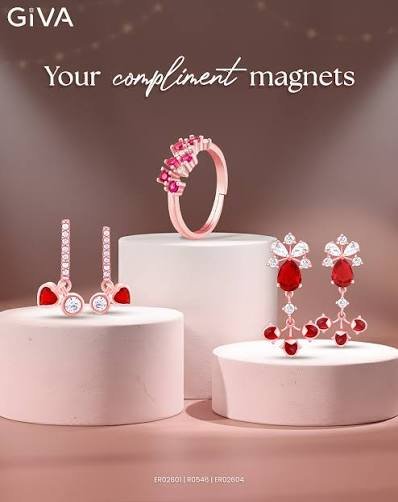 A GIVA campaign layout titled 'Your compliment magnets', featuring a rose-toned ring, ruby heart-drop earrings, and a floral-motif drop set on pale pedestals